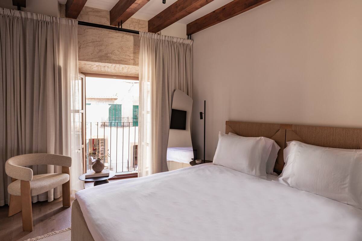 Un dormitorio con una cama grande, cabecera de madera, una silla y vistas a un balcón con cortinas.
