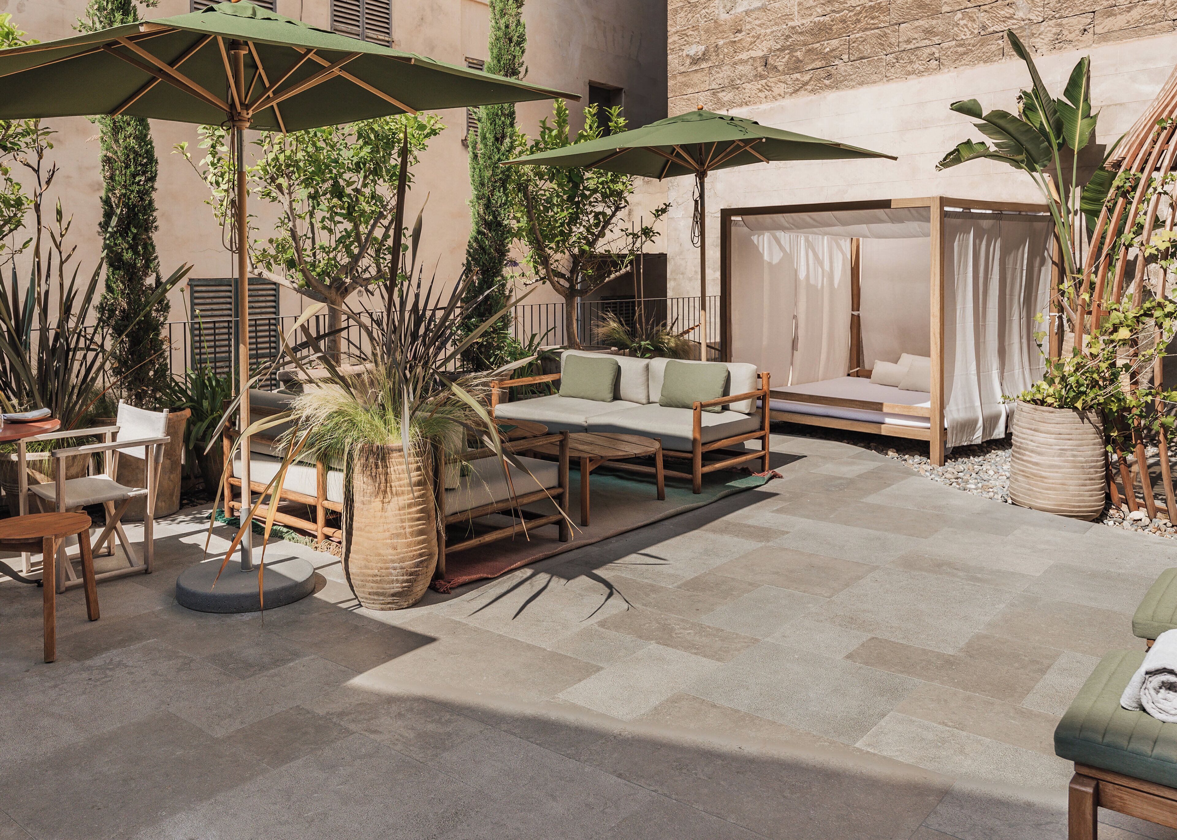 An outdoor seating area with a sofa, chairs, and a table, surrounded by potted plants and umbrellas.