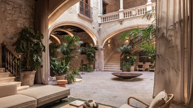 Un patio espacioso con zona de estar, numerosas plantas en macetas y una fuente central.