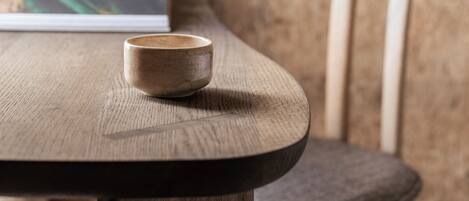 A wooden table with a cup, a laptop, and a chair in a room with a textured wall and a lamp.