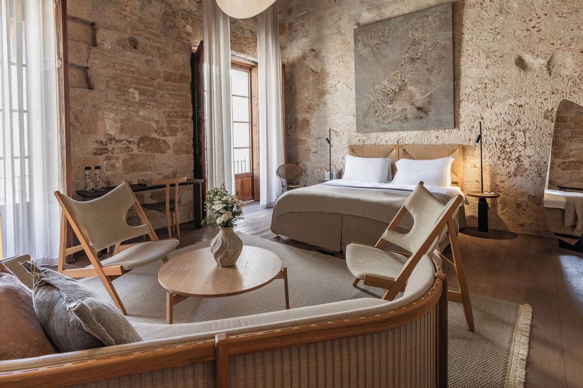 Una habitación acogedora con cama, dos sillas, una mesita y un ventanal grande.