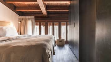 A bedroom with a wooden ceiling, a bed with a beige blanket, a bedside table, and a wicker basket.
