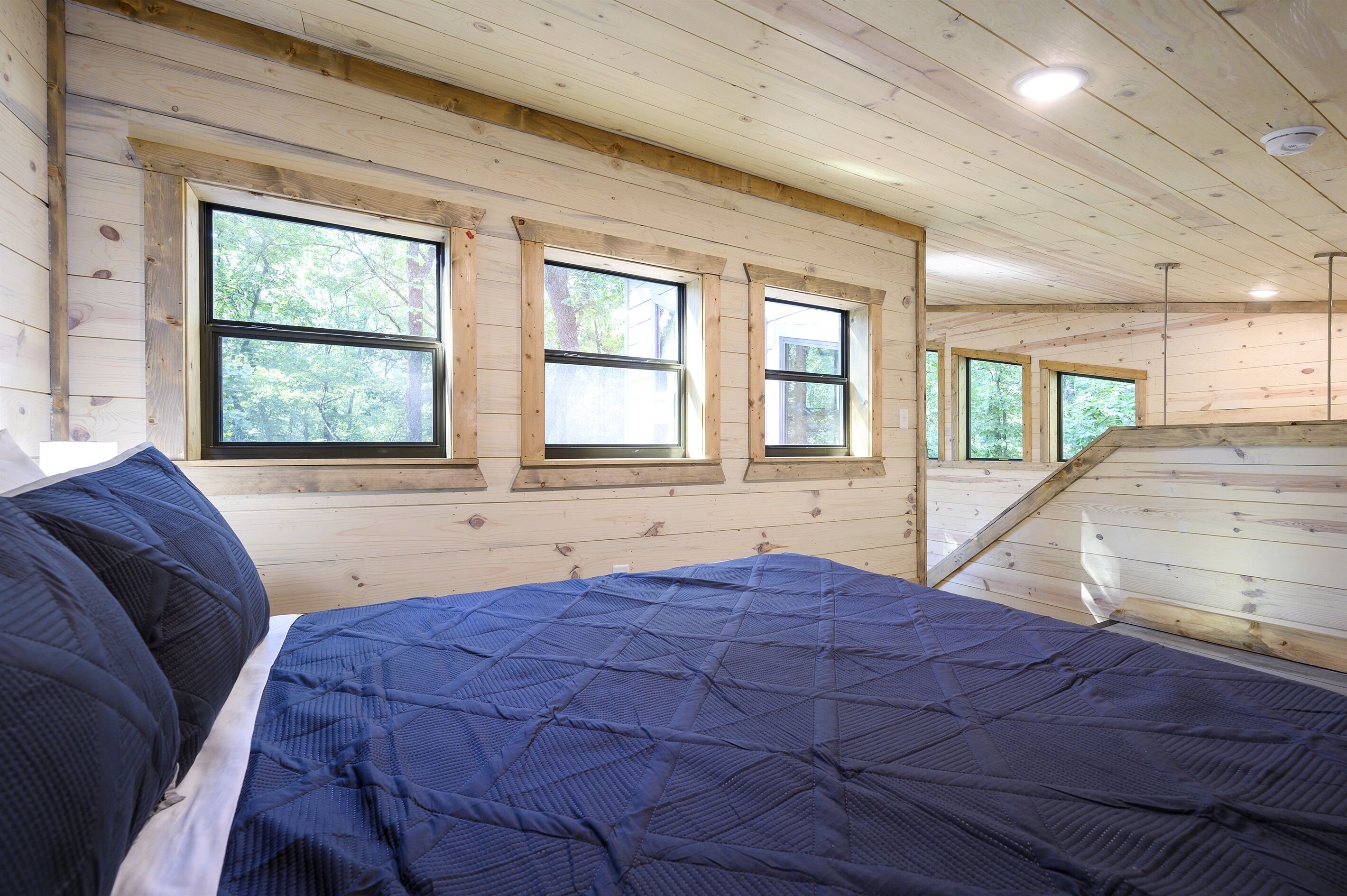 Een slaapkamer met een bed, houten wanden en drie ramen.