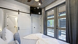 Un dormitorio con cama, televisor montado y puerta corrediza de vidrio que da a un espacio al aire libre.