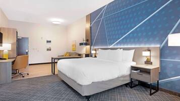 A hotel room with a large bed, a desk with a chair, a small table, and a wall with a geometric pattern.
