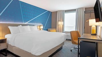 Habitación de hotel con una cama grande, un escritorio, una silla, un televisor y una ventana con cortinas.