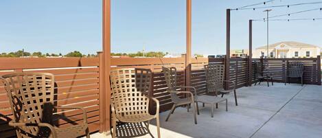 Outdoor seating with metal chairs and a wooden fence, a clear sky, and a building in the background.