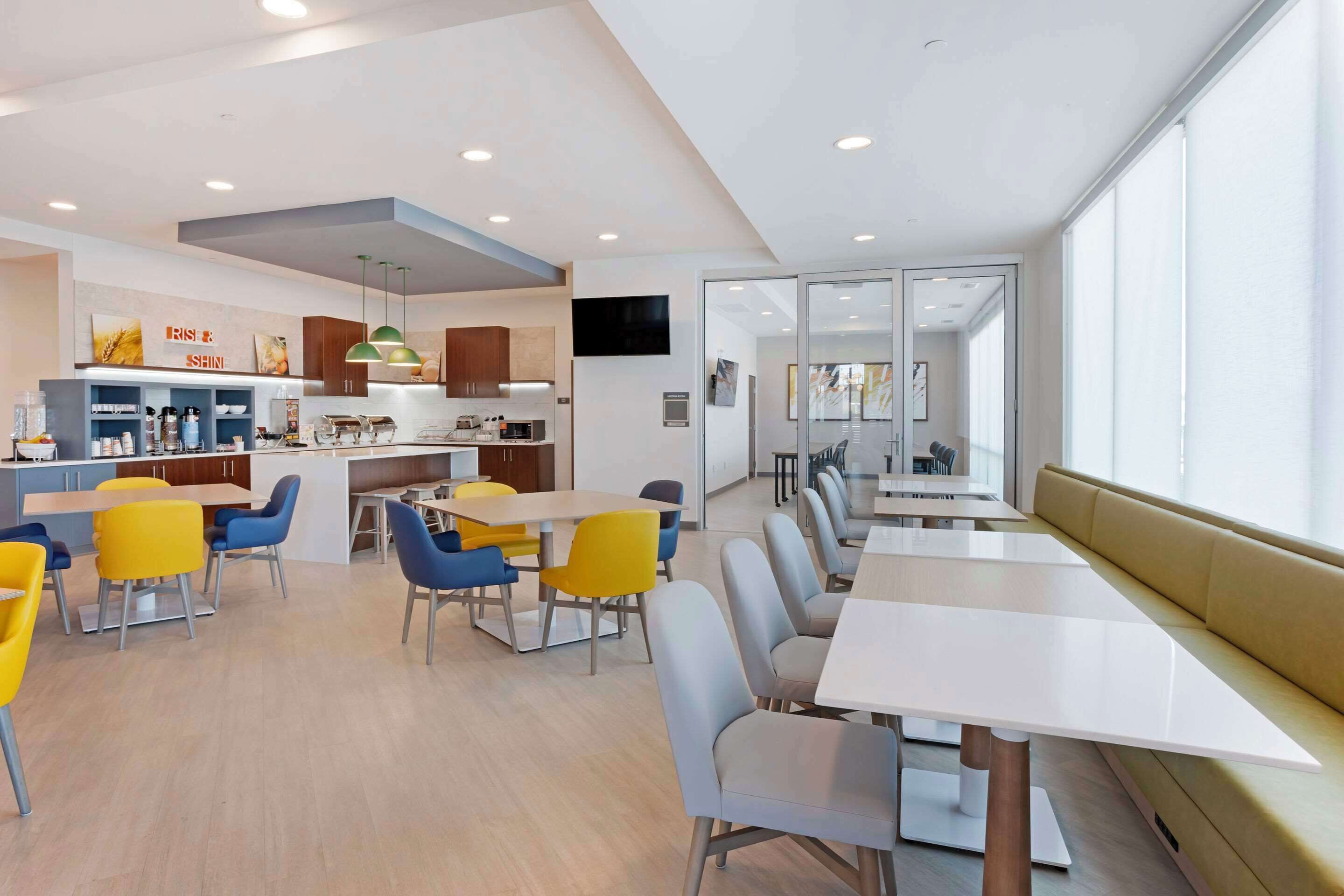 A modern dining area with yellow and blue chairs, a white table, and a kitchen area with a counter and cabinets.
