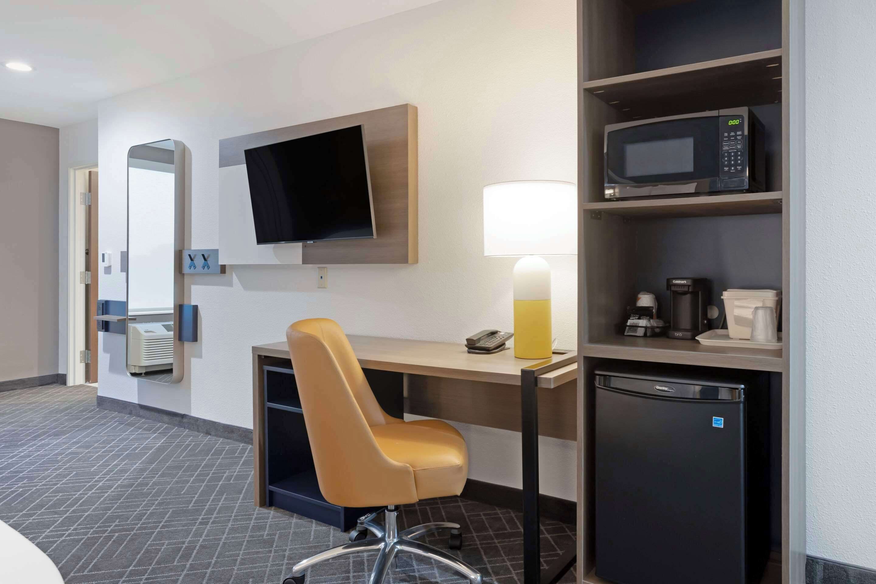 Ein Hotelzimmer mit Schreibtisch, Stuhl, Fernseher, Mikrowelle, Minikühlschrank und Spiegel.