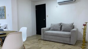 A living room with a grey sofa, a white chair, a dining table with chairs, and a black door.
