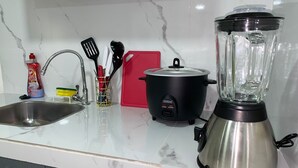 A kitchen with a sink, a red cutting board, a black slow cooker, and a stainless steel blender.