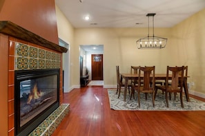 Un coin repas avec une table et des chaises en bois, une cheminée agrémentée de carreaux décoratifs et un lustre.