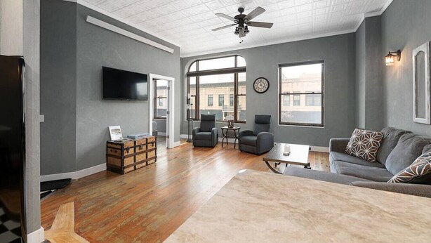 A spacious living room with hardwood floors, a gray couch, a coffee table, and a ceiling fan. - Downtown Spearfish Loft East (Spearfish)