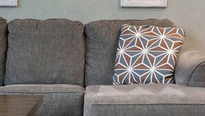 A grey sectional sofa with a geometric patterned pillow against a wall with framed mirrors. - Downtown Spearfish Loft East (Spearfish)