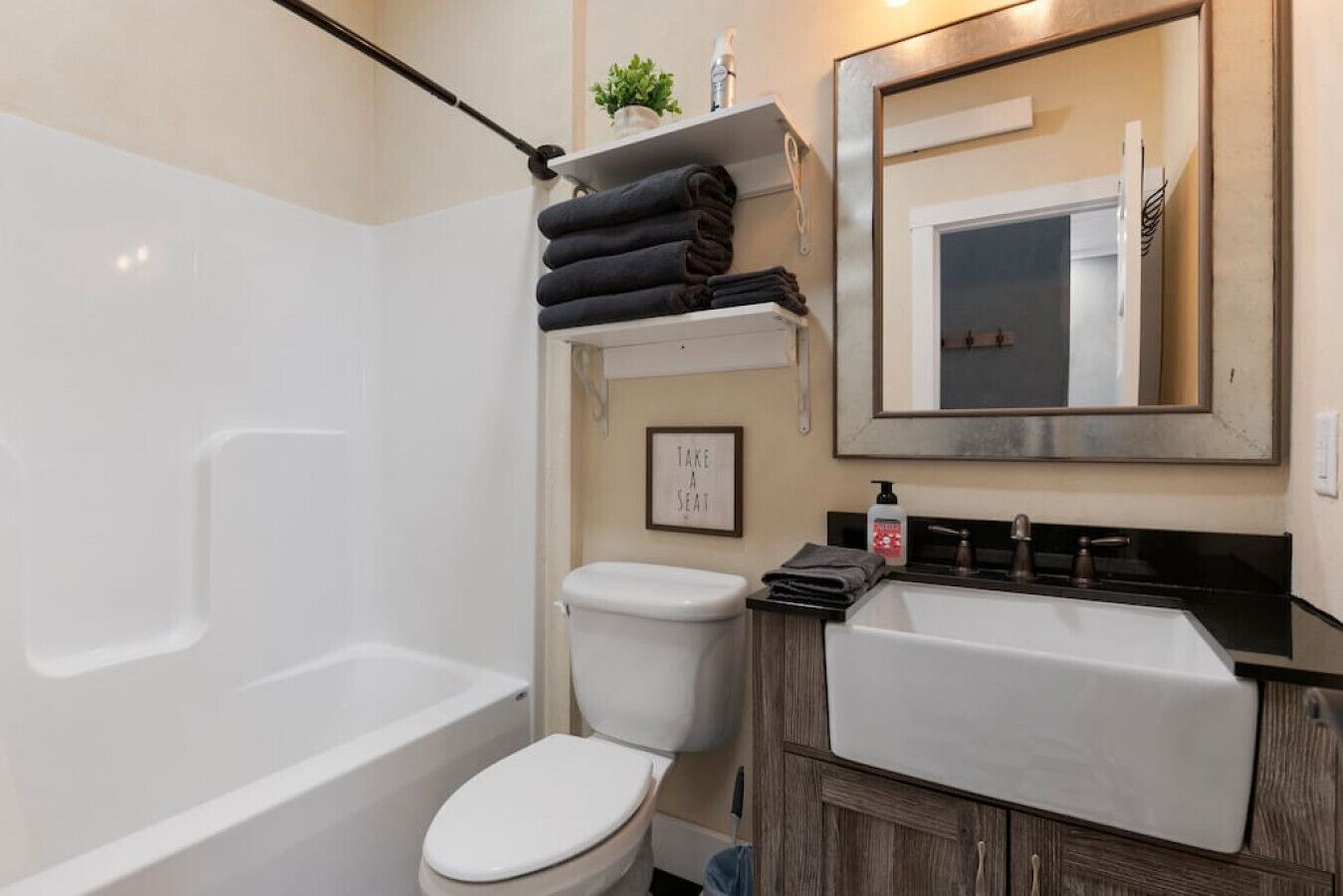 A bathroom with a bathtub, toilet, and sink. There is a towel rack with folded towels, a framed sign, and a mirror above the sink.