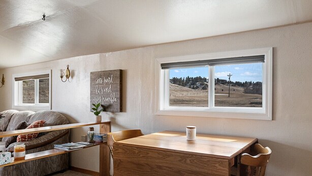 Una sala de estar acogedora con una mesa de comedor de madera, un sofá y un ventanal con vistas a un paisaje montañoso.