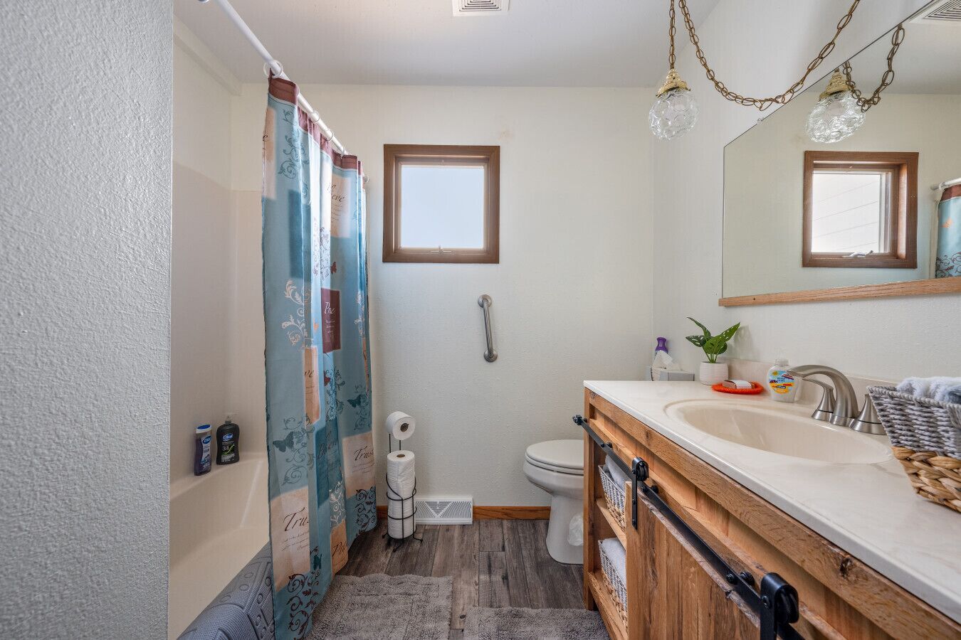 Une salle de bain avec un meuble-lavabo en bois, un évier, des toilettes et un rideau de douche.