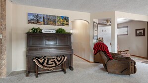 Un pasillo con una consola de madera oscura con el rótulo "FARMHOUSE", un tapete estampado y un sillón de cuero marrón con una manta roja y negra.