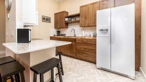 A compact kitchen with a marble countertop, wooden cabinets, a white refrigerator, and a 'eat' sign on the wall. - Downtown Spearfish Loft West (Spearfish)