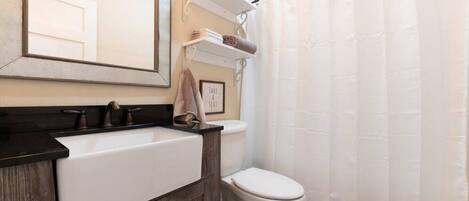 A bathroom with a white sink, dark wood vanity, a toilet, a shower curtain, and a framed sign on the wall.