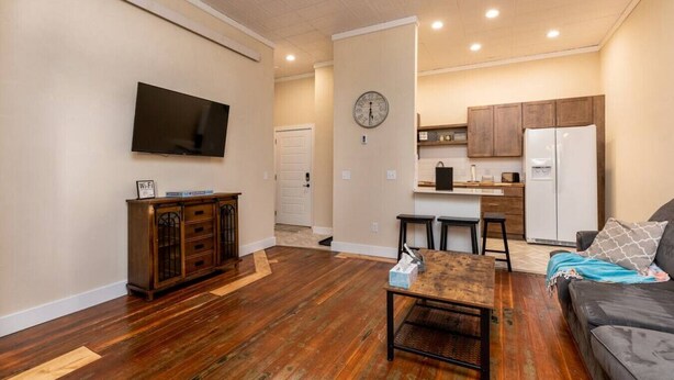 A living room with a TV, wooden furniture, a kitchen with a fridge, and a clock on the wall. - Downtown Spearfish Loft West (Spearfish)