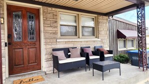 Ein Haus mit einer Steinaußenseite, einer Holztür und einer Veranda mit Korbmöbeln und Kissen.