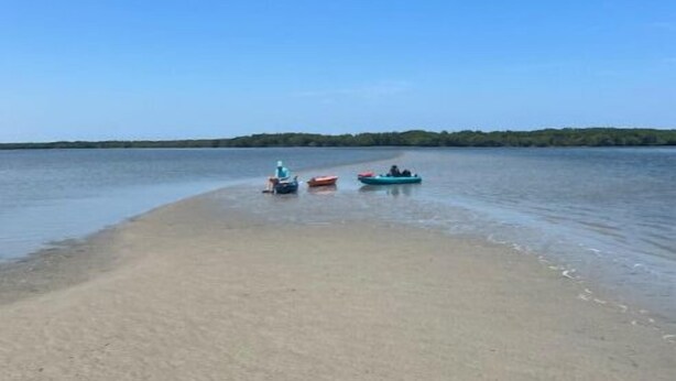 Een strand met een heldere lucht en rustig water. Er liggen drie boten aan de kust.