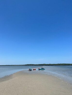 A beach with a clear sky and calm water. There are three boats on the shore.
