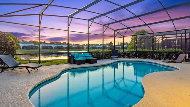 Área de piscina com piscina em curva, espreguiçadeiras e um espaço de estar coberto com vista para casas e um corpo de água.