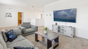 Uma sala de estar moderna com um sofá cinzento, uma mesa de centro e uma televisão na parede.