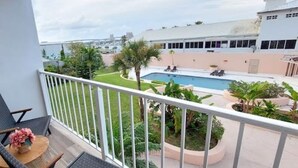 En balkon med udsigt over en swimmingpool, en stol og et lille bord med en vase.