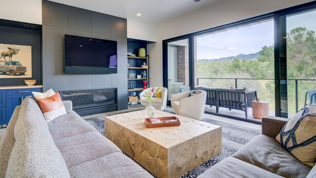 Un salon moderne doté d’un grand téléviseur, de sièges confortables, d’une table basse et d’un balcon offrant une vue sur la verdure.