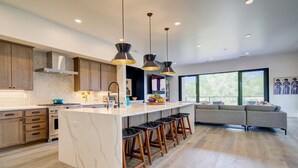 Une cuisine moderne dotée d’un grand îlot central, de tabourets de bar en bois et de luminaires suspendus.