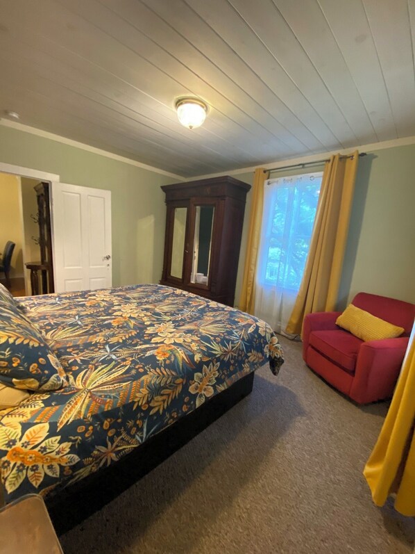 Un dormitorio con una cama grande, una silla roja, un armario de madera y una ventana con cortinas.