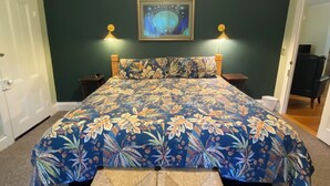 Une chambre à coucher avec un grand lit, un banc, deux tables de chevet et un tableau accroché au mur.