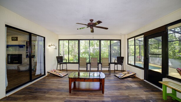 A spacious room with a ceiling fan, large windows, and a wooden coffee table. - Haven at Rainbow Springs: Kayaks, Pool, Game Room (Dunnellon)