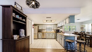 A modern kitchen with wooden cabinets, a coffee machine, and a bar area with stools. - Haven at Rainbow Springs: Kayaks, Pool, Game Room (Dunnellon)