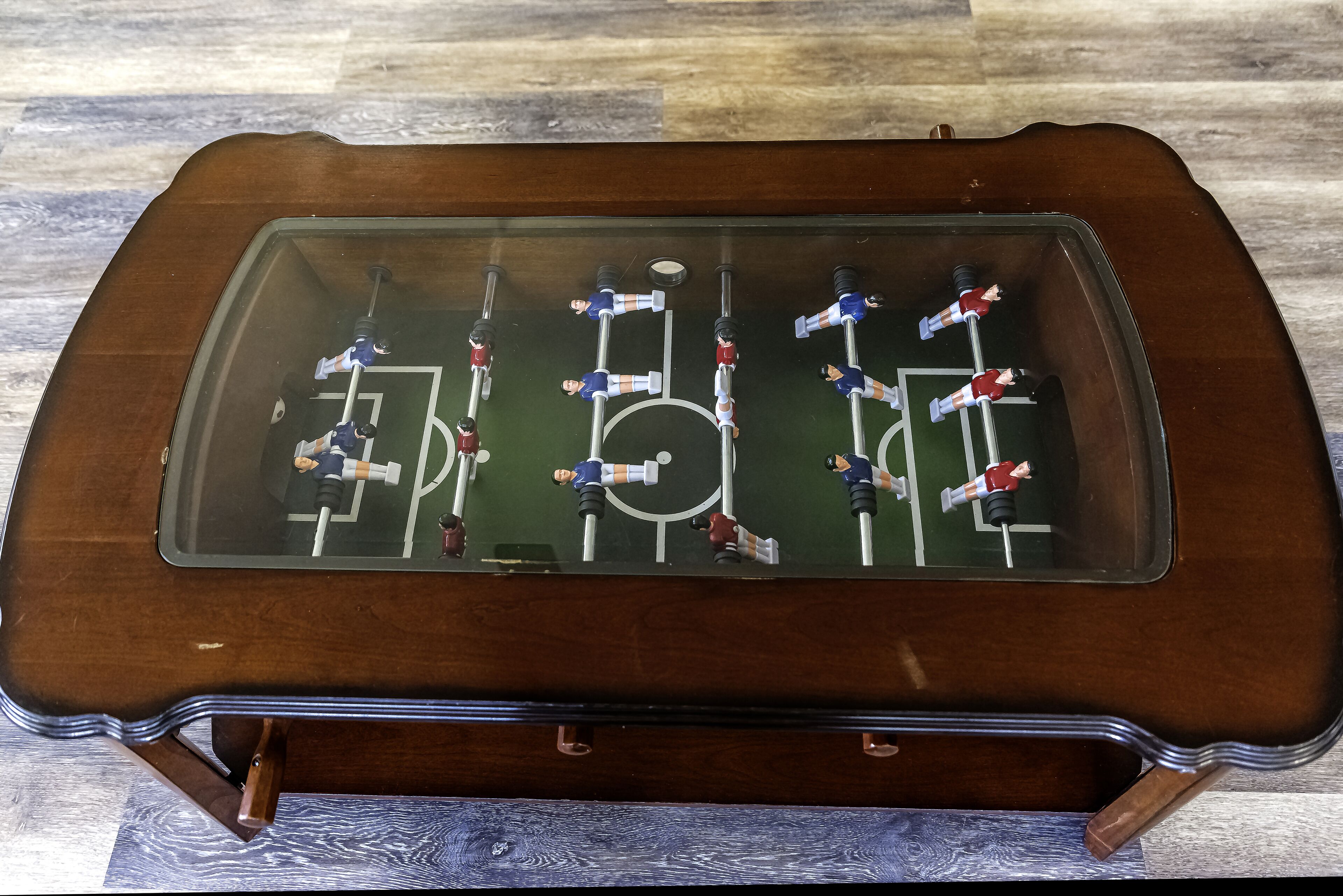 A tabletop foosball table with a glass top and wooden base.
