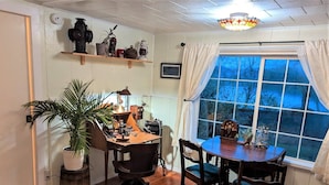 A cozy room with a wooden desk, a large window with curtains, a potted plant, and a vintage radio. - Ticketmaster Chamber - Historic Lakefront Studio Cabin with Kayaking (oregon)