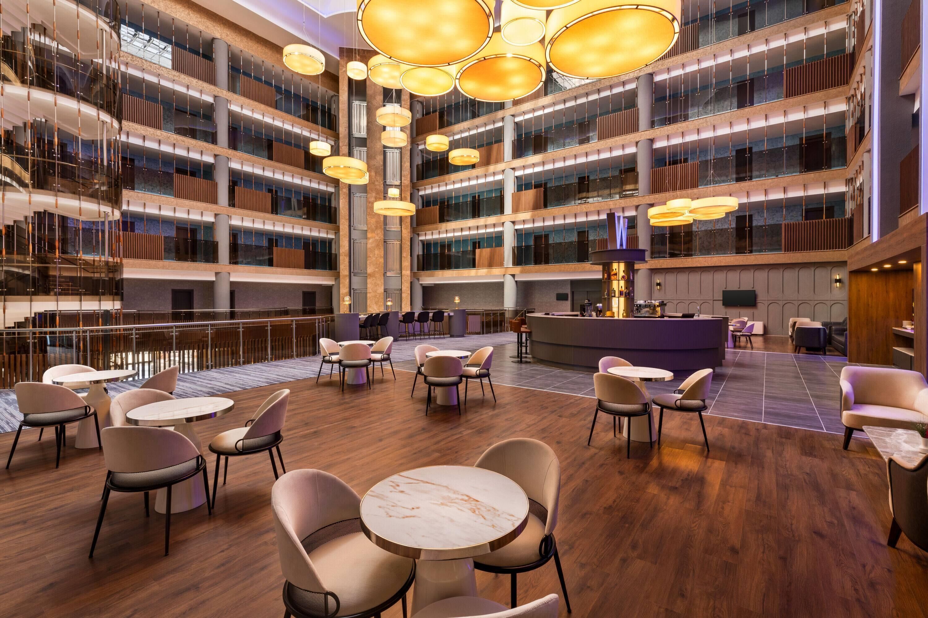 A multi-level hotel lobby with a central bar area, seating arrangements, and a modern chandelier design.