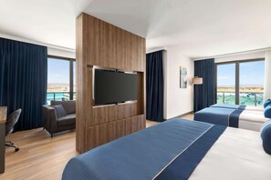 Une chambre d’hôtel dotée d’un grand lit, d’un téléviseur fixé sur un panneau en bois, d’un bureau avec une chaise, et offrant une vue sur la ville et les montagnes.