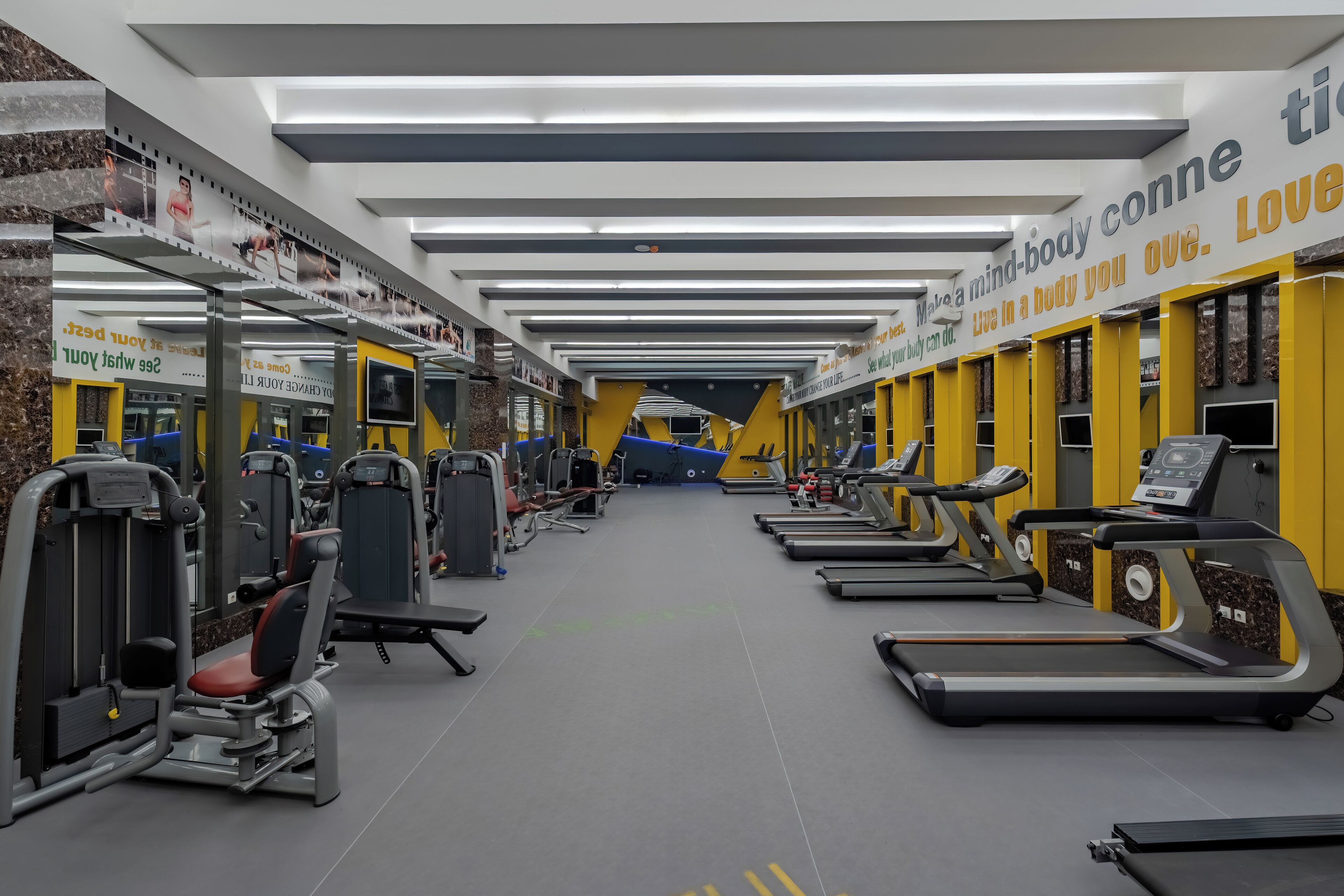 Un gimnasio con cintas de correr, máquinas de pesas y espejos.