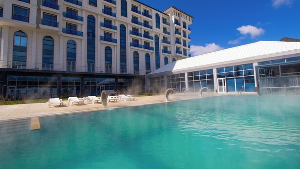 A hotel with a swimming pool, lounge chairs, and a large building with multiple windows and balconies.