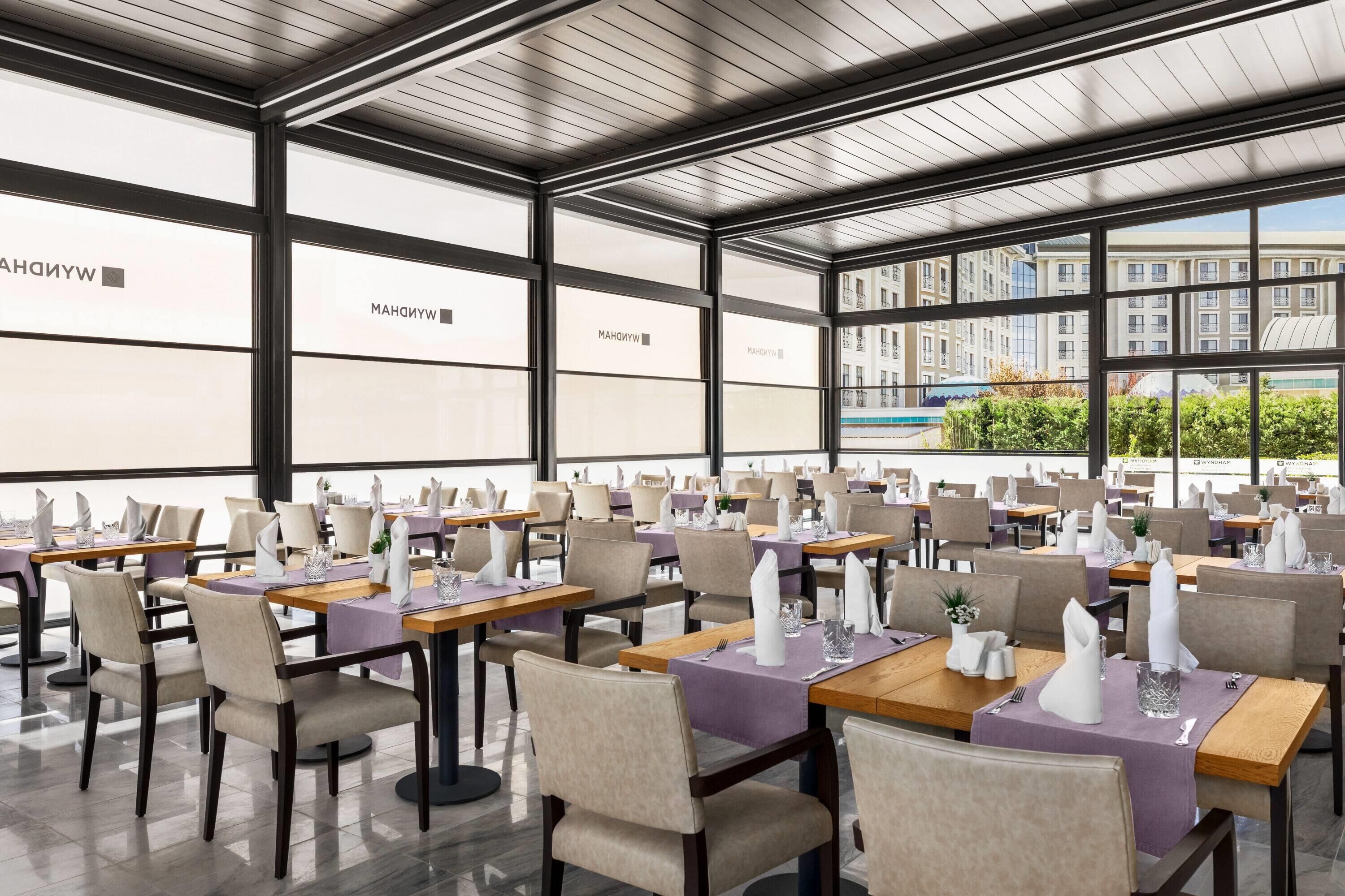 Un restaurante con mesas dispuestas para comer, ventanas amplias y vistas a edificios.
