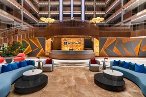 A modern lobby with a reception desk, seating areas, and a high ceiling with lighting fixtures.