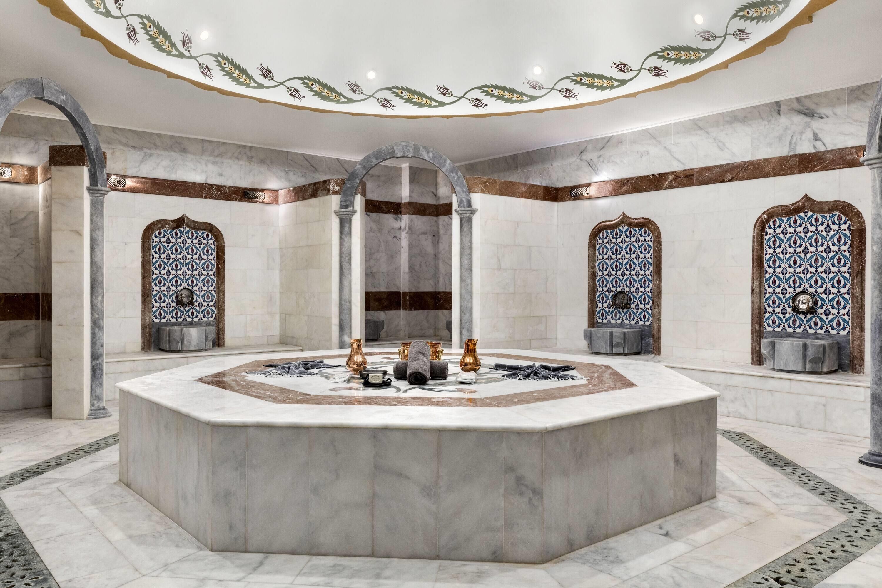 Un baño lujoso con un lavamanos central de mármol, intrincados diseños de azulejos y elementos arquitectónicos clásicos.