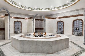 A luxurious bathroom with a central marble sink, ornate tile patterns, and classical architectural elements.