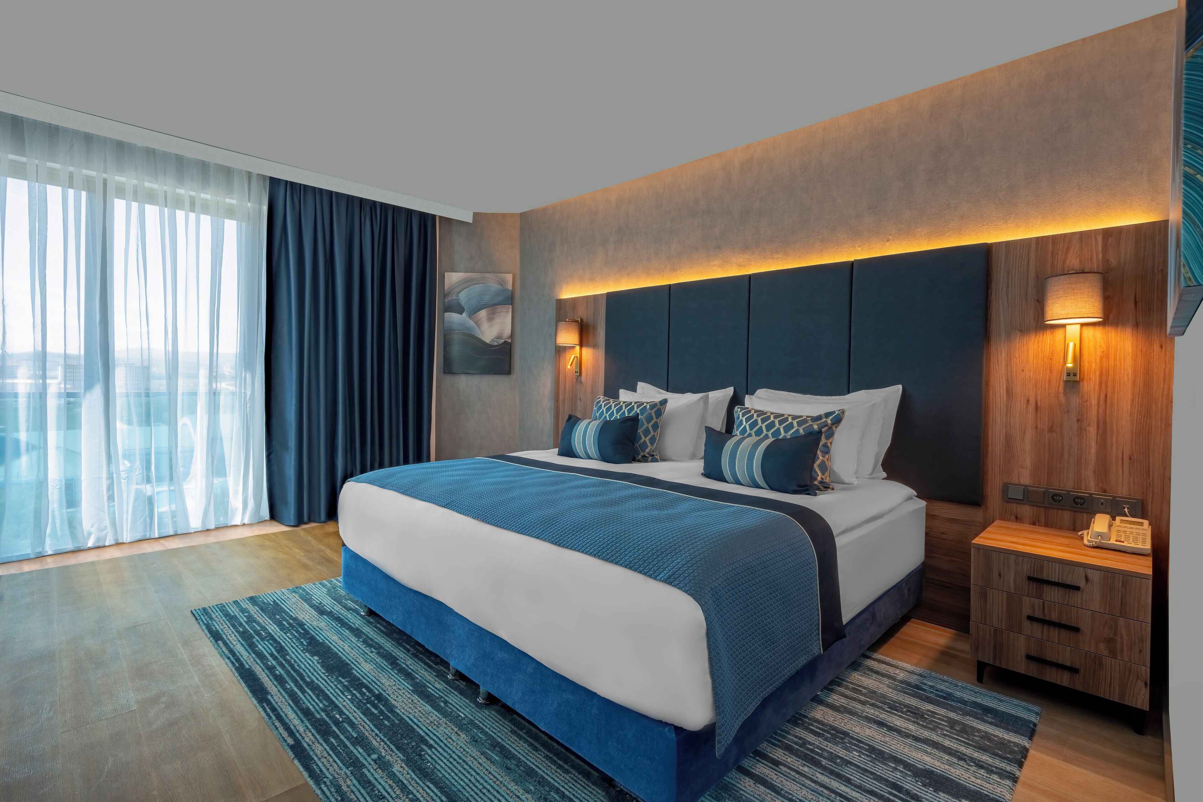 A modern hotel room with a large bed, a wooden headboard, and a nightstand with a lamp.