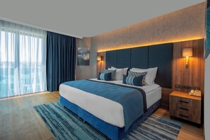 Een moderne hotelkamer met een groot bed, een houten hoofdeinde en een nachtkastje met een lamp.