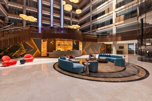 Un moderno vestíbulo de hotel con un área de estar central, un mostrador de recepción y una gran pantalla digital.